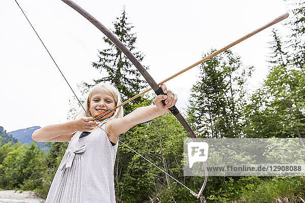 Smiling girl aiming with bow and arrow in the nature