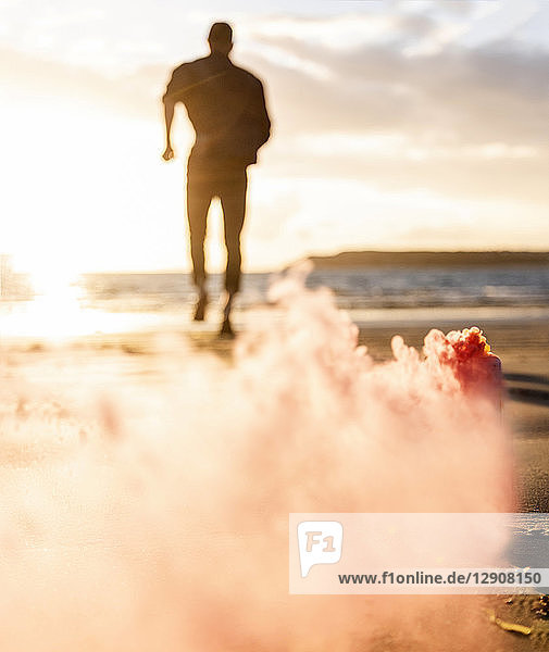 Young man running on the beach at sunset with colorful smoke