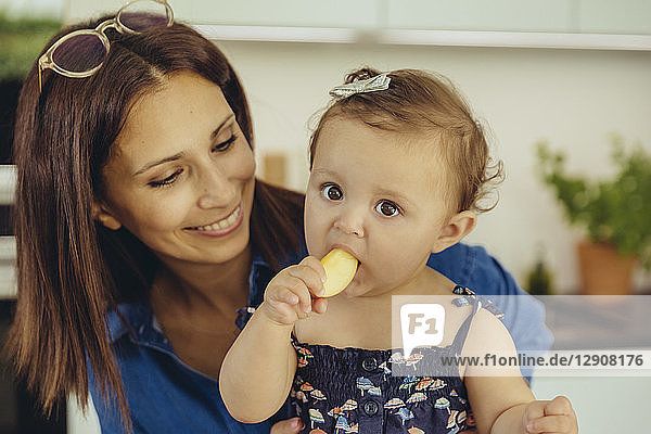 Mother watching baby daughter eating an apple