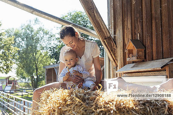 Happy mother and little daughter sitting in straw in a barn