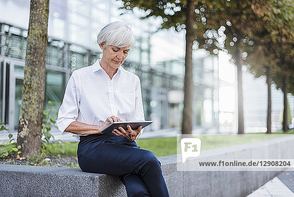 Senior businesswoman sitting outside using tablet