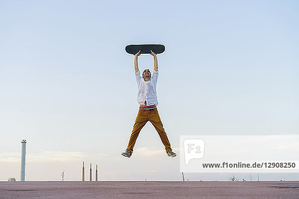 Young man jumping in the air holding a skateboard