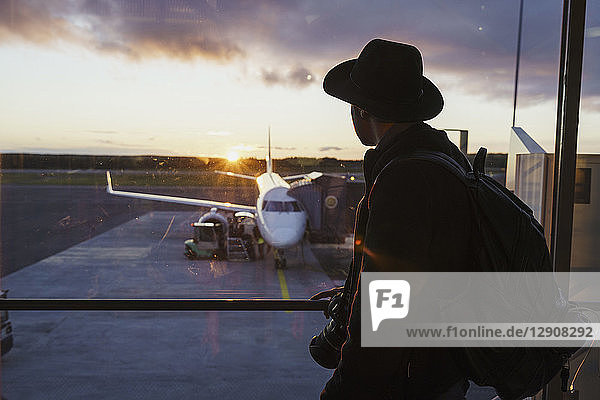 Young man with hat and backpack looking through window on plane at the airport