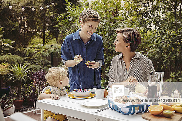 Two happy mothers at breakfast table outdoors with their child
