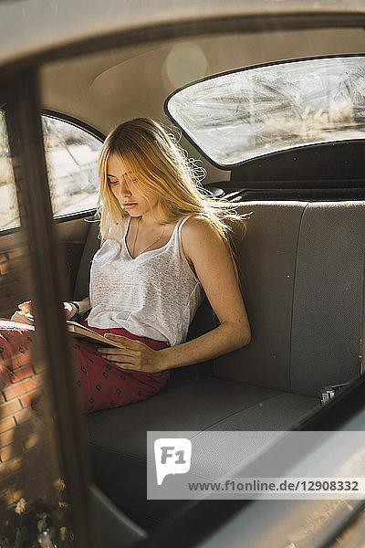 Young woman sitting in a car reading book