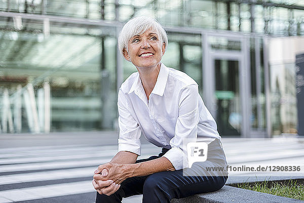 Smiling senior businesswoman sitting outside looking around