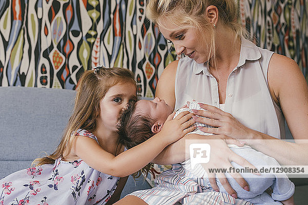 Smiling mother sitting on couch with newborn baby and daughter