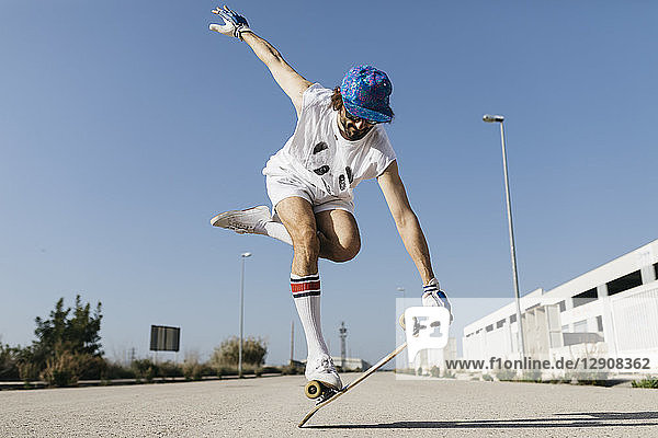 Man in stylish sportive outfit standing on skateboard against blue sky