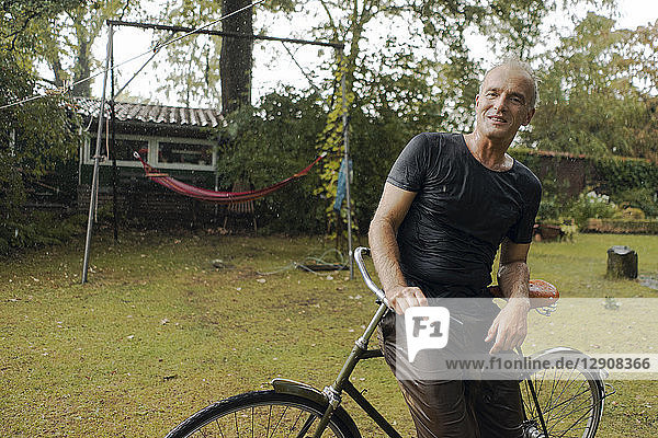 Portrait of mature man with bicycle in summer rain in garden