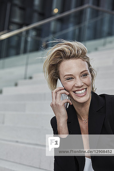 Portrait of laughing businesswoman on the phone sitting on stairs outdoors