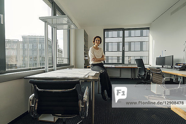 Successful businesswoman sitting on desk in her office