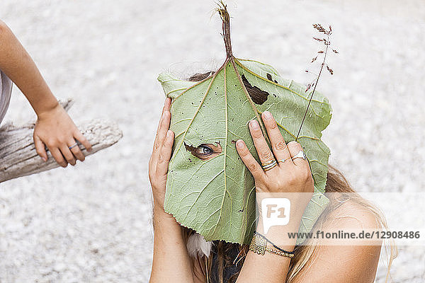Playful woman peeking through hole in large leaf
