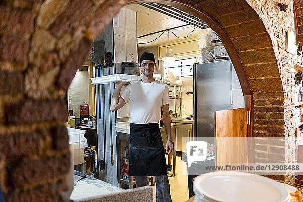 Portrait of smiling pizza baker holding a box in kitchen
