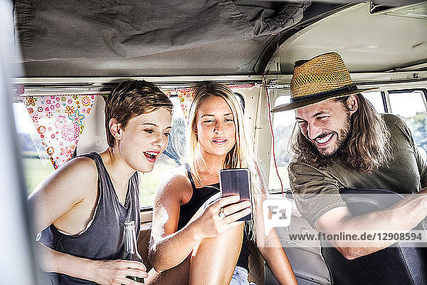 Happy friends inside van looking at smartphone