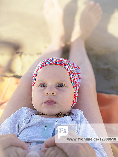 Portrait of baby girl lying on mother's legs on the beach