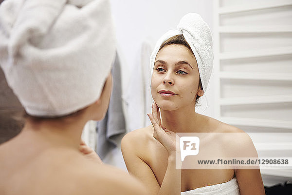 Mirror image of young woman examining her face in the bathroom