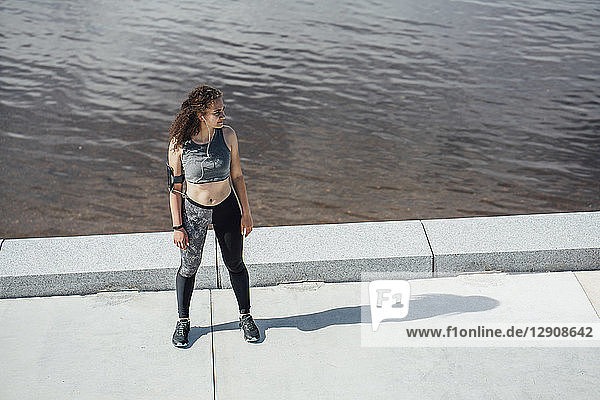 Young athletic woman wearing earbuds standing at the riverside