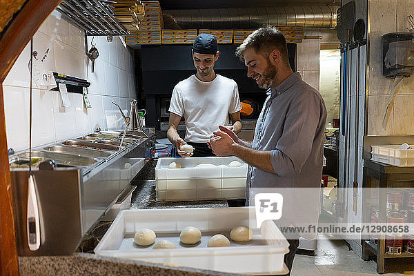Two men with raw dough in boxes in kitchen of a pizzeria