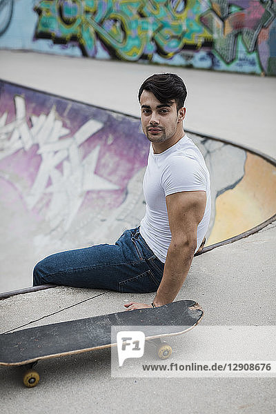 Portrait of young man with skateboard sitting in skatepark