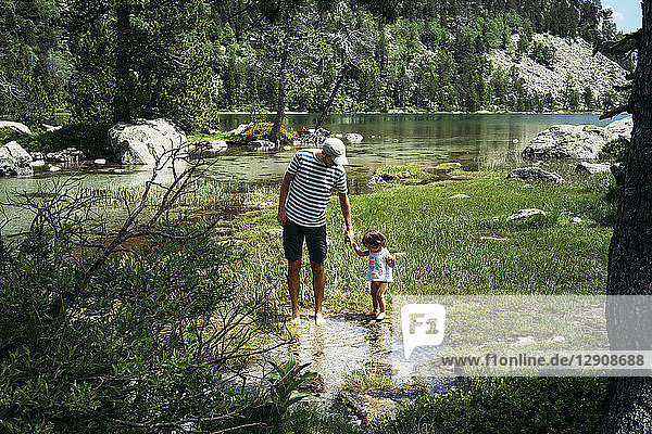 Spain  Father and daughter exploring mountain lake  standing ankle deep in water