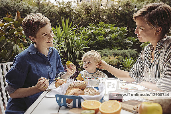 Two happy mothers at breakfast table outdoors with their child