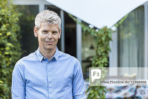 Portrait of content mature man with grey hair in front of his house