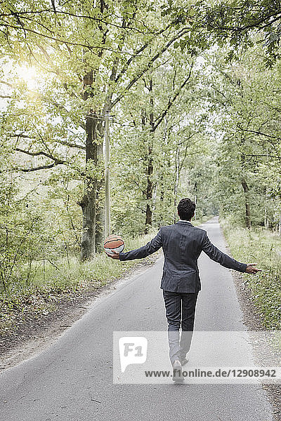 Rear view of businessman walking with basketball on rural road