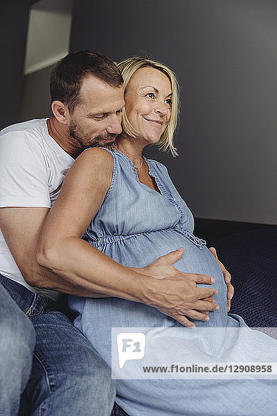Mature man and his pregnant mature wife sitting on bed touching her belly