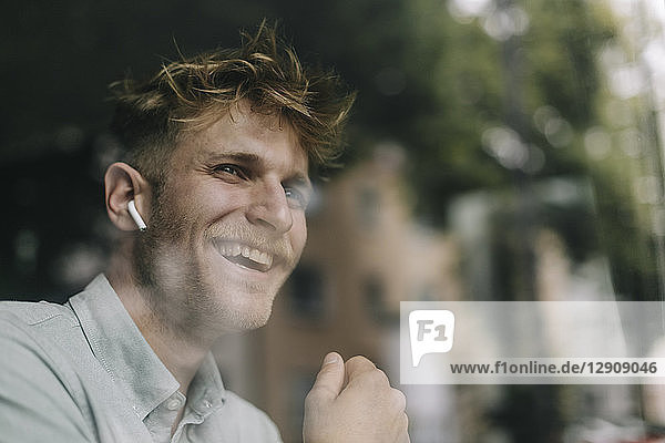 Young man standing at the window  using ear buds  laughing