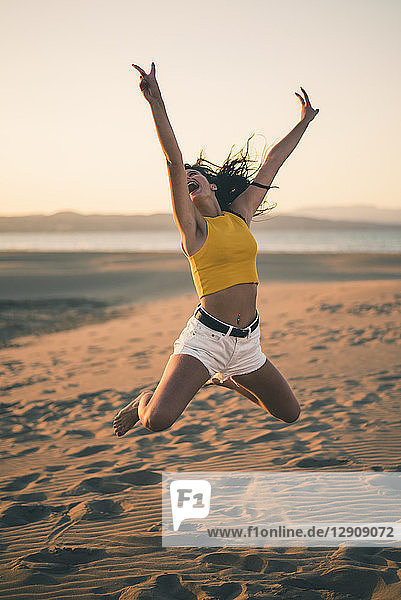 Happy teenage girl jumping in the air on the beach at sunset