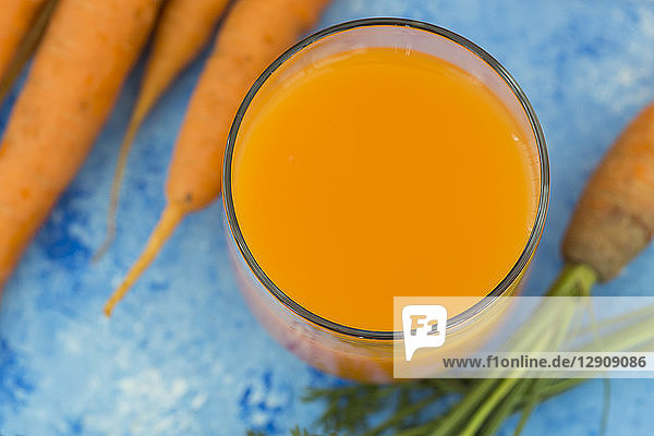 Glass of fresh carrot juice and carrots on light blue ground