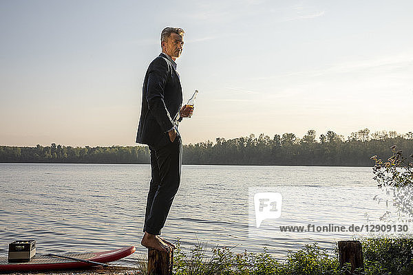 Businessman with beverage standing barefoot on a pole at lake