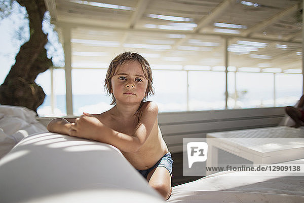 Portrait of serious little boy resting at lounge on the beach