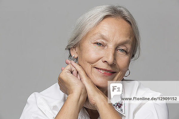 Portrait of relaxed senior woman with grey hair in front of grey background