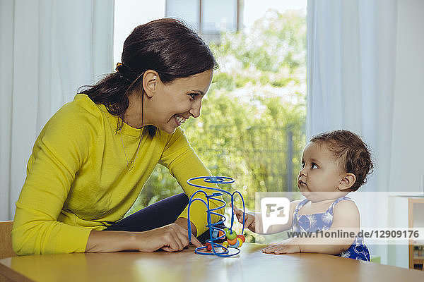 Happy mother and baby daughter playing with motoric loop