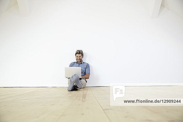 Mature man sitting on ground in empty room  using laptop