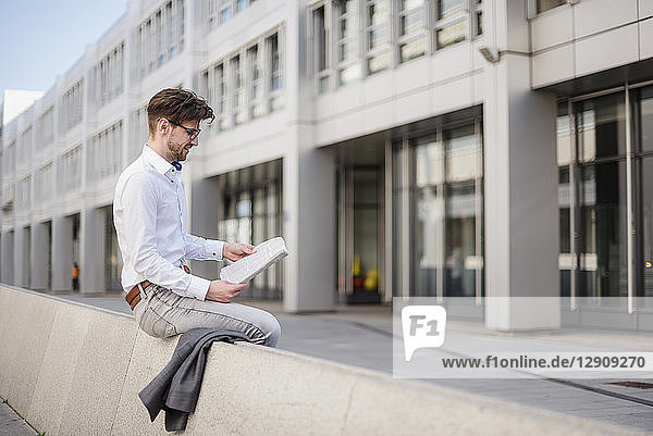 Businessman sitting in the city reading newspaper