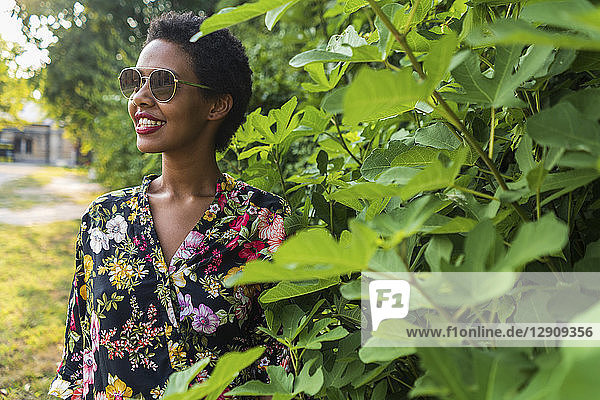 Smiling young woman wearing sunglasses and colourful blouse in a park