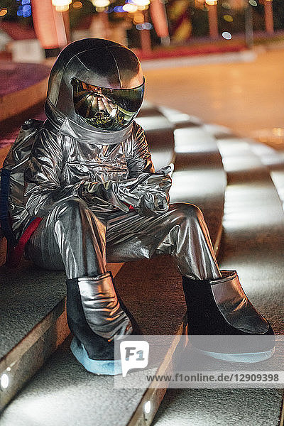 Spaceman sitting on illuminated stairs at night using cell phone