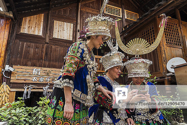 China  Guizhou  three Miao women wearing traditional dresses and headdresses using cell phone