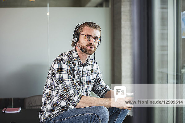 Casual businessman with cup of coffee and headset in office