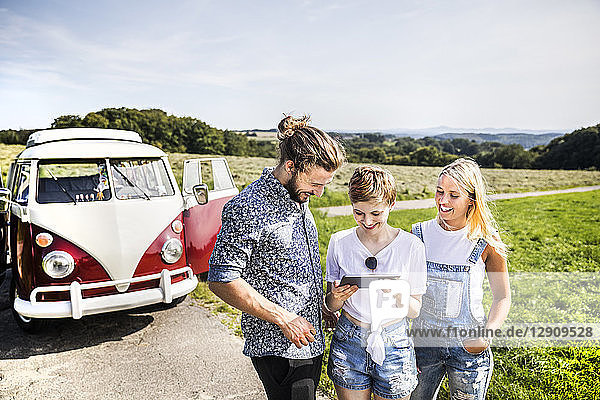 Happy friends outside van in rural landscape looking at tablet