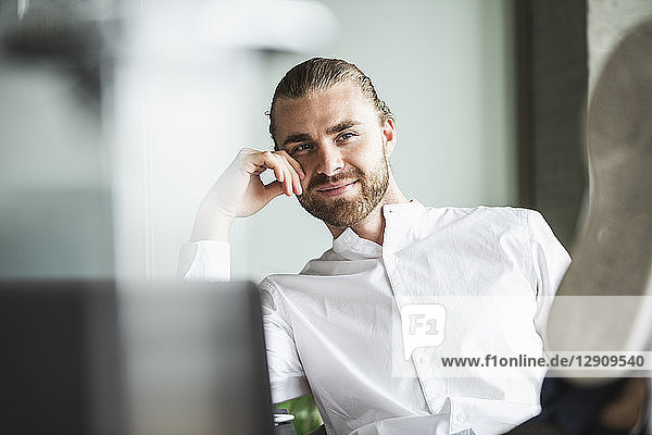 Portrait of smiling businessman sitting in office with feet up