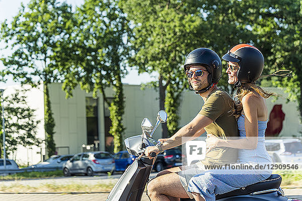 Happy couple riding motor scooter in summer