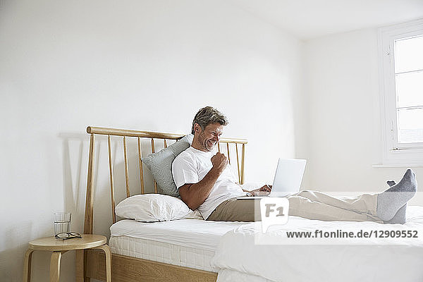 Mature man enjoying success with laptop in bed