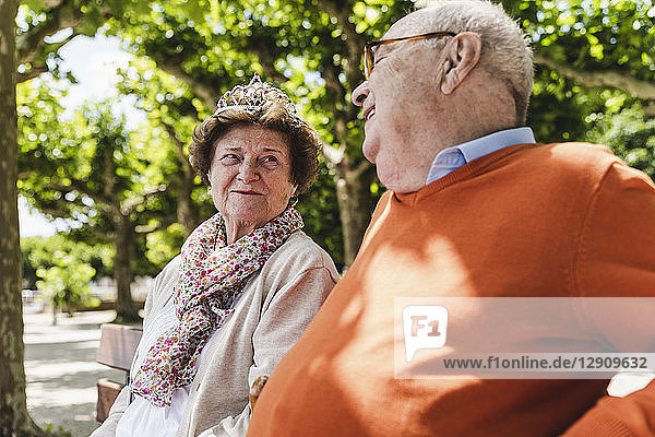 Happy senior couple sitting in park  woman wearing crown