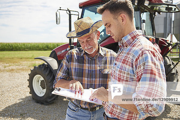 Two farmers looking at data from clipboard on the farm