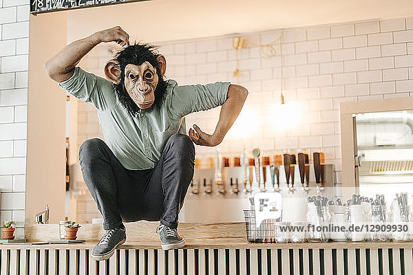 Man wearing monkey mask  sitting on counter of a bar  scratching head