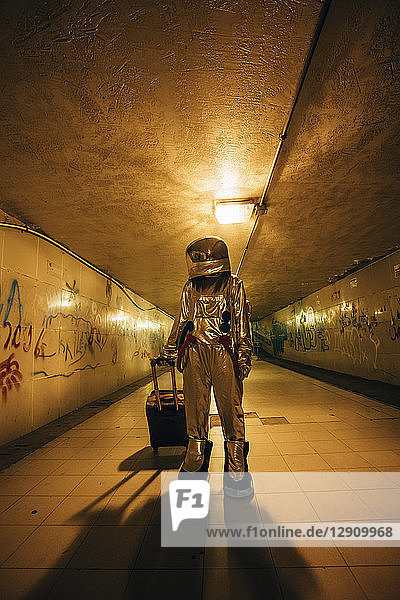Spaceman in the city at night standing in underpass with rolling suitcase