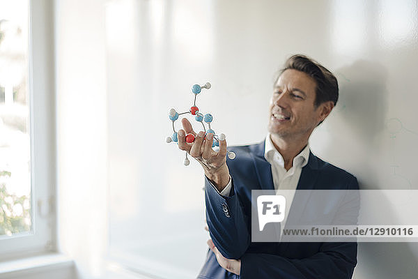 Successful businessman leaning on whiteboard  holding molecule model